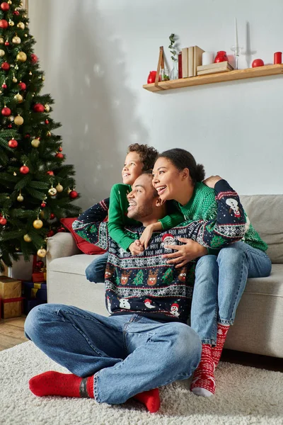 Tiro vertical de alegre família afro-americana abraçando calorosamente sentado ao lado da árvore de Natal — Fotografia de Stock