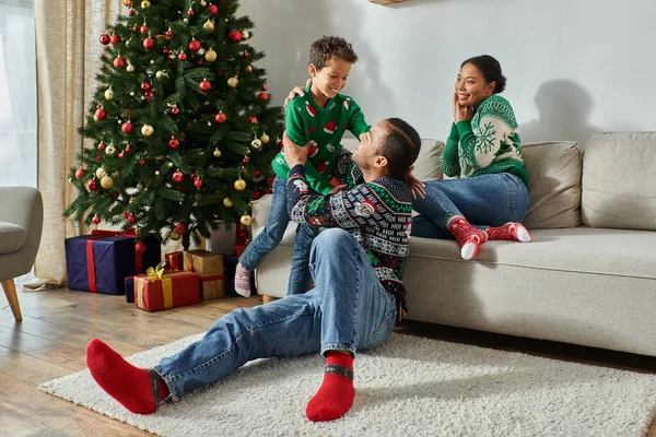 Bonita mulher americana africana olhando alegremente para seu marido e filho ao lado da árvore de Natal — Fotografia de Stock