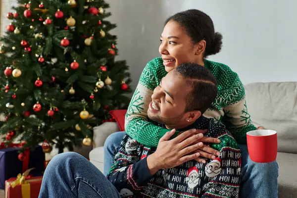 Happy african american couple hugging warmly with coffee cup in hand, looking away, Christmas — Stock Photo