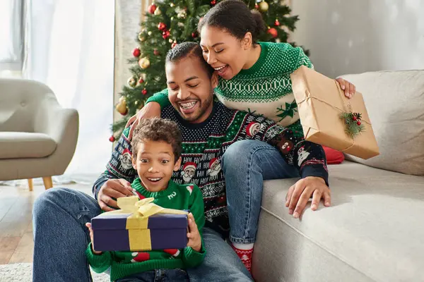Familia afroamericana alegre asombrada abrazándose y mirando sorprendida en regalo de Navidad - foto de stock