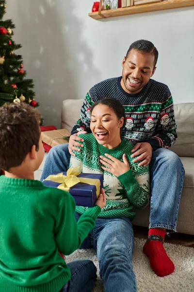 Vertical shot of jolly african american parents hugging and receiving gift from their son, Christmas — Stock Photo