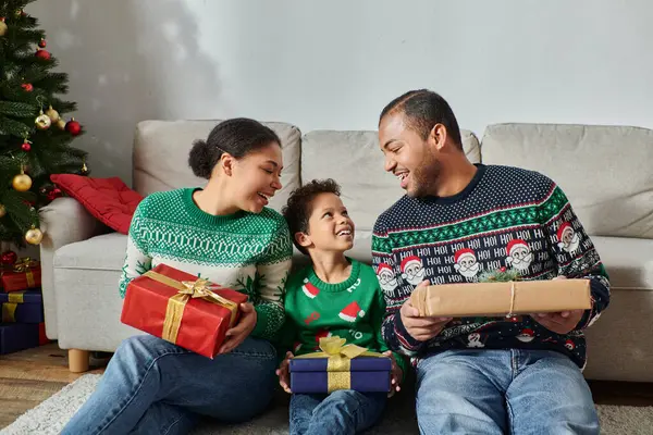 Joyeux parents afro-américains regardant avec amour leur fils et tenant des cadeaux, Noël — Photo de stock