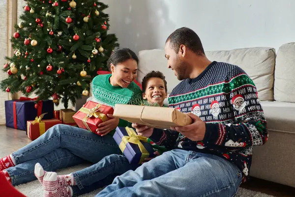 Happy african american family sitting on floor holding presents and smiling cheerfully, Christmas — Stock Photo