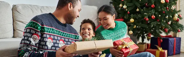 Heureuse famille afro-américaine assise sur le sol avec des cadeaux et souriant joyeusement, Noël, bannière — Photo de stock