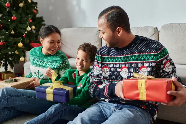 Joyeuse famille afro-américaine assis à côté de l'arbre de Noël avec des cadeaux dans leurs mains — Photo de stock