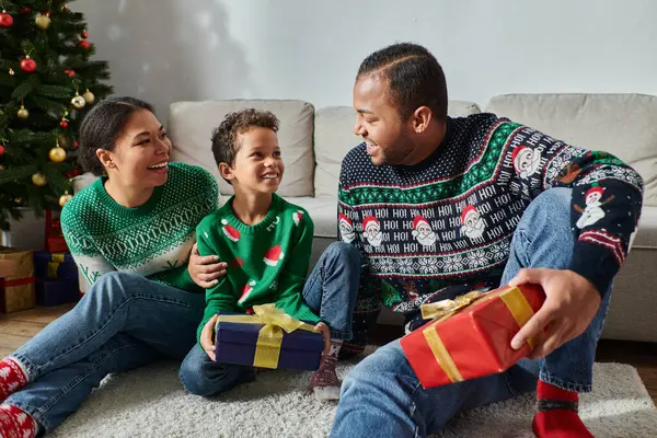 Gut aussehender afrikanisch-amerikanischer Vater hält Geschenk in der Hand und lächelt seinem Sohn und seiner Frau zu, Weihnachten — Stockfoto