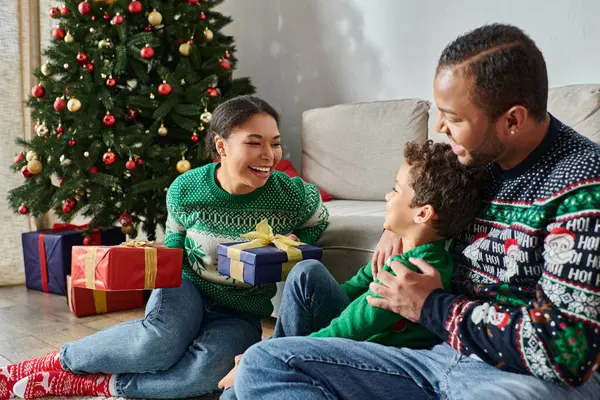 Freudige afrikanisch-amerikanische Familie in warmen Pullovern auf dem Boden sitzend Geschenke austauschend, Weihnachten — Stockfoto