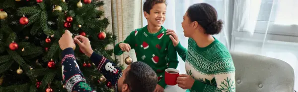 Joyeuse femme afro-américaine regardant son fils et son mari décorer arbre de Noël, bannière — Photo de stock