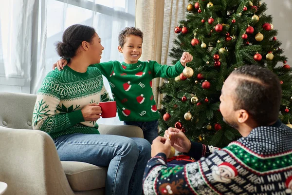 Freudige afrikanisch-amerikanische Eltern, die ihren Sohn liebevoll dabei beobachten, wie er den Weihnachtsbaum mit Kugeln schmückt — Stockfoto