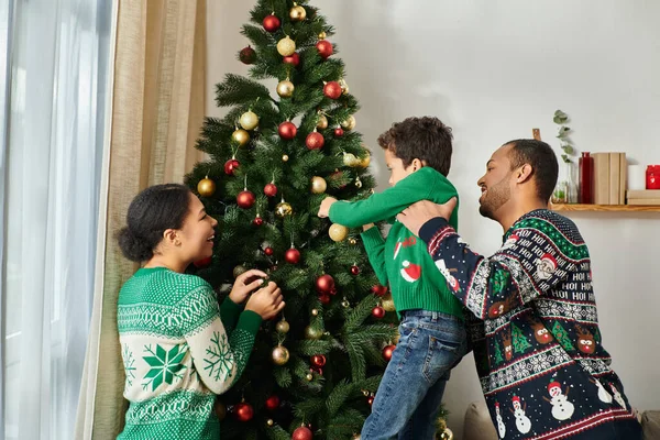 Glücklich schöne afrikanisch-amerikanische Familie in gemütlichen Pullovern schmücken Weihnachtsbaum mit Kugeln — Stockfoto