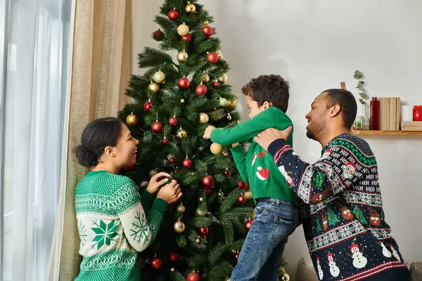 Happy beautiful african american family in cozy sweaters decorating Christmas tree with baubles — Stock Photo
