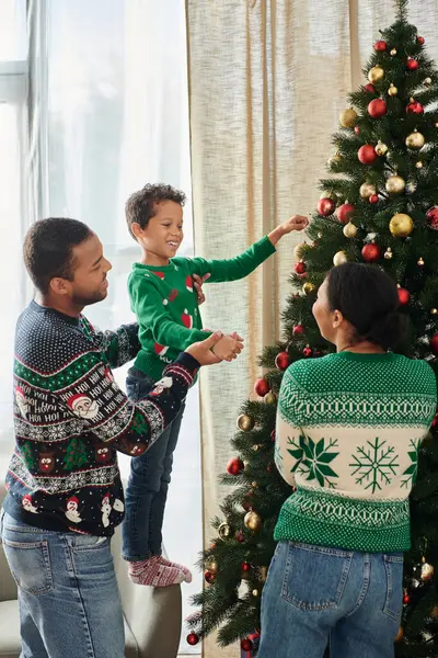 Plan vertical de famille afro-américaine souriant joyeusement à l'autre décoration arbre de Noël — Photo de stock