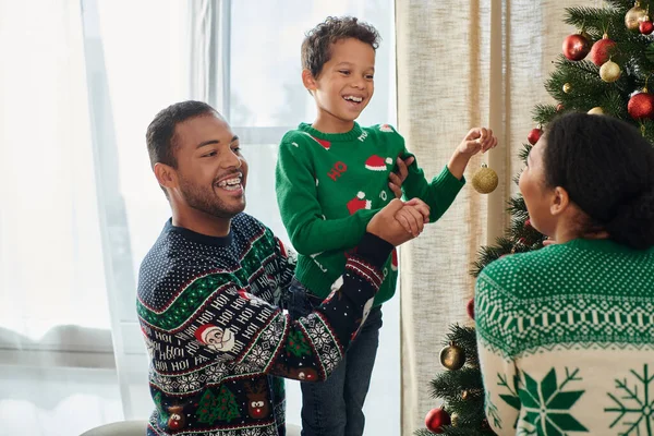Heureux afro-américain homme aider fils décorer arbre de Noël et sourire joyeusement à sa femme — Photo de stock