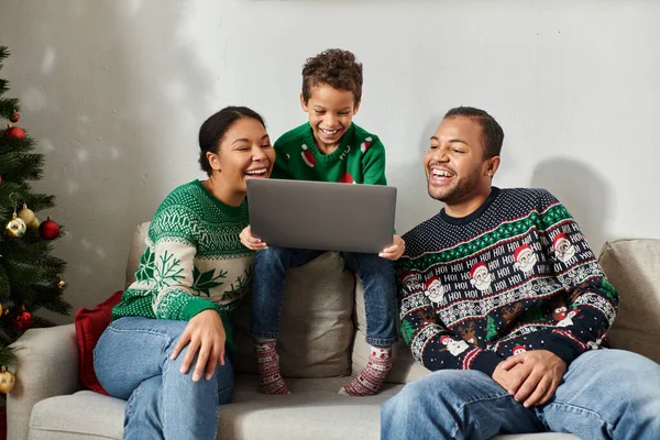 Happy african american family in warm sweaters sitting on sofa watching Christmas movie on laptop — Stock Photo
