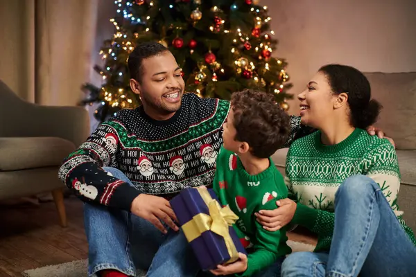Joyeux homme afro-américain regardant joyeusement son fils et sa femme assis sur le sol près de l'arbre de Noël — Photo de stock
