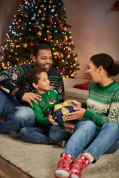 Vertikale Aufnahme einer glücklichen afrikanisch-amerikanischen Frau, die ihrem Sohn und Ehemann ein Weihnachtsgeschenk macht — Stockfoto