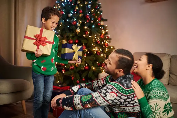 Felici genitori afro-americani guardando amorevolmente il loro simpatico figlio in possesso di regali, Natale — Foto stock