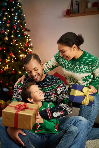 Vertikale Aufnahme süßer afrikanischer amerikanischer Junge hält Geschenk in der Hand und lächelt seine Eltern an, Weihnachten — Stockfoto