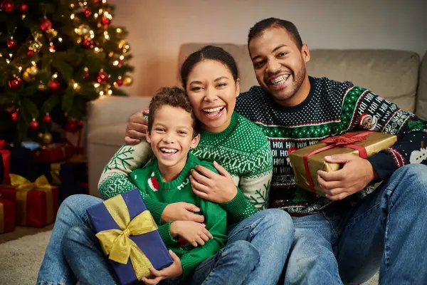 Felice famiglia afro-americana che abbraccia calorosamente accanto all'albero di Natale e sorride allegramente alla macchina fotografica — Foto stock
