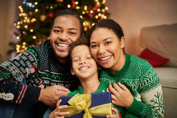 Portrait de la famille afro-américaine heureuse dans des pulls chauds étreignant et souriant à la caméra, Noël — Photo de stock