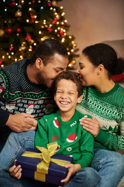 Vertical shot of joyous african american parents hugging and kissing their cheerful son, Christmas — Stock Photo