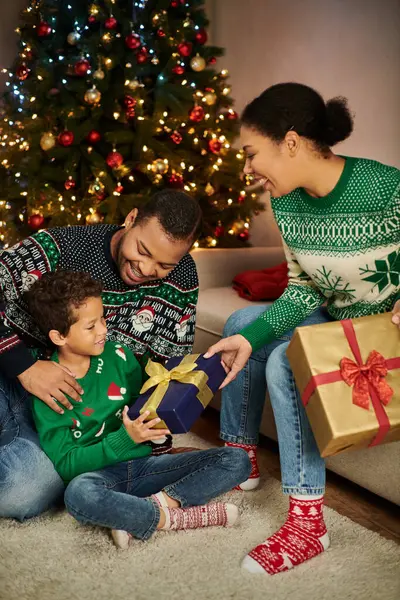 Plan vertical de mère afro-américaine donnant un cadeau à son fils pendant que son père l'étreint, Noël — Photo de stock