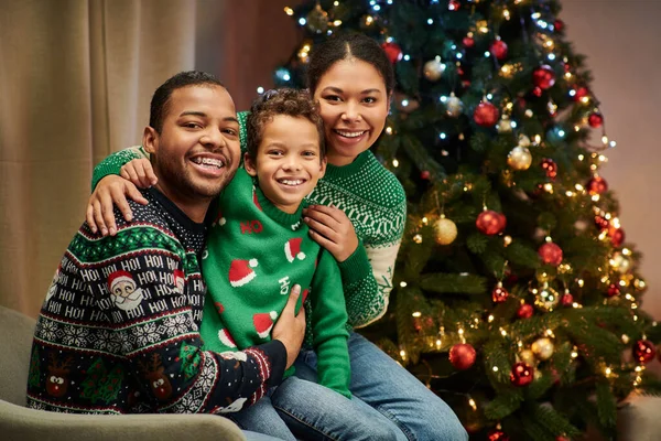 Moderna famiglia afroamericana in maglioni caldi sorridenti alla macchina fotografica mentre abbraccia calorosamente, Natale — Foto stock