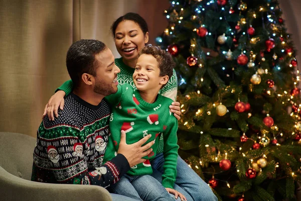Moderne fröhliche afrikanisch-amerikanische Familie, die sich vor Weihnachtsbaumkulisse glücklich anlächelt — Stockfoto