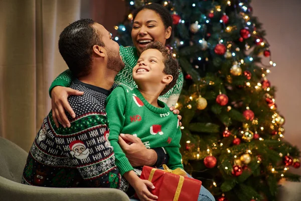 Alegre família afro-americana abraçando calorosamente e sorrindo um para o outro alegremente, Natal — Fotografia de Stock