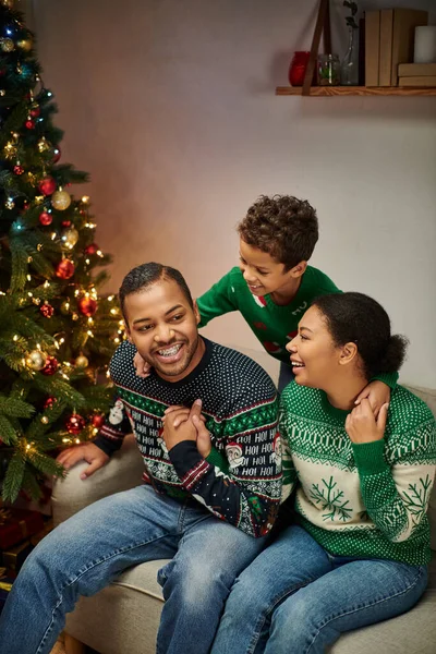 Disparo vertical de alegres padres afroamericanos mirando amorosamente a su hijo sosteniendo regalo de Navidad - foto de stock