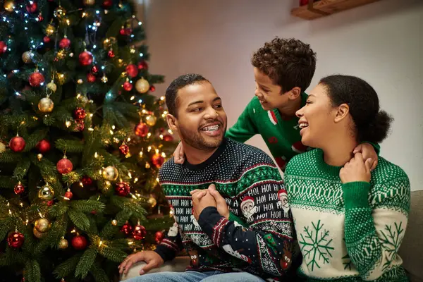 Moderne joyeux afro-américain famille étreignant et souriant à l'autre par le sapin de Noël — Photo de stock