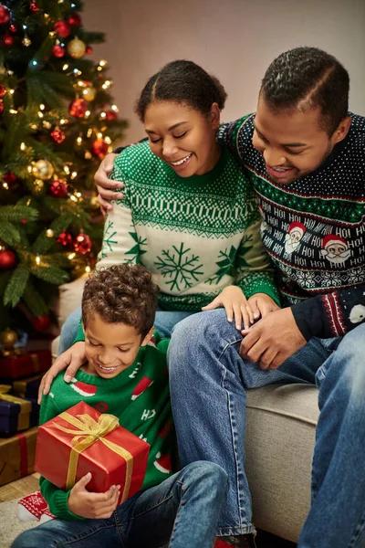 Vertical shot of joyful african american parents looking lovingly at son holding Christmas present — Stock Photo