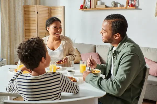 Felice famiglia afro-americana in abiti casual sorridenti amorevolmente a vicenda durante la colazione — Foto stock