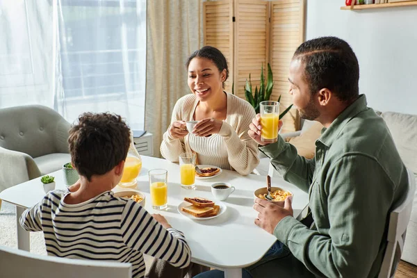 Allegra famiglia afro-americana moderna che fa colazione insieme e si sorride — Foto stock