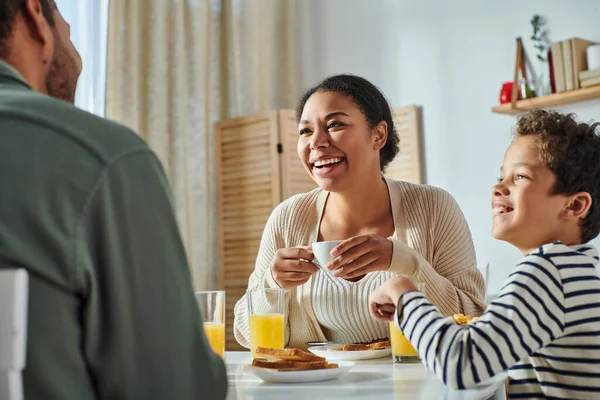 Cropped view of african american man smiling at his beautiful wife and son at breakfast table — Stock Photo