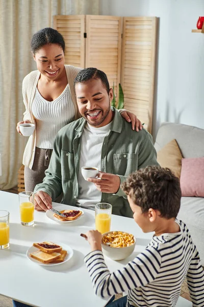Vertical focused shot of jolly african american parents looking happily at their blurred son — Stock Photo