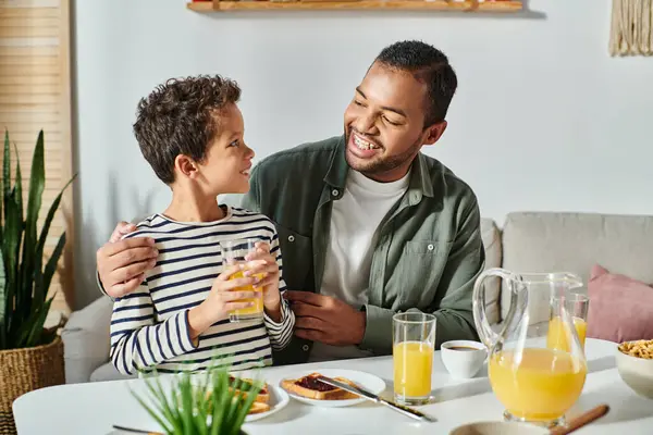 Cheerful african american father and son in homewear smiling at each other during breakfast — Stock Photo