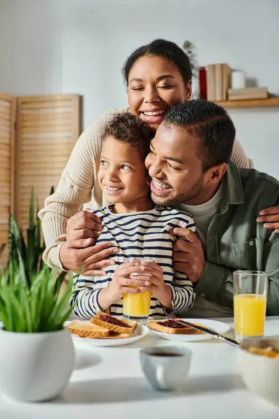 Vertical shot of cheerful african american family hugging warmly each other at breakfast table — Stock Photo