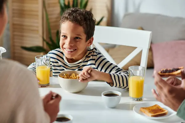 Африканские американские родители завтракают вместе со своим веселым маленьким сыном, который ест кукурузные хлопья — стоковое фото