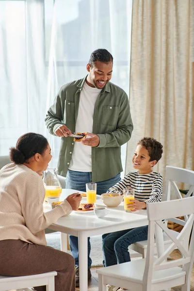 Plano vertical de la hermosa familia afroamericana sonriendo felizmente desayunando delicioso - foto de stock