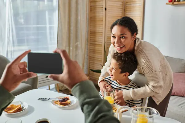 Vue recadrée de l'homme afro-américain prenant en photo sa femme gaie et son fils à la table du petit déjeuner — Photo de stock
