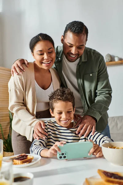 Colpo verticale di adorabile piccola famiglia afro-americana guardando il telefono cellulare a colazione — Foto stock