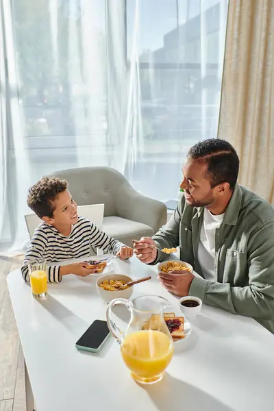 Vertical shot of joyful african american father and son enjoying breakfast and smiling happily — Stock Photo