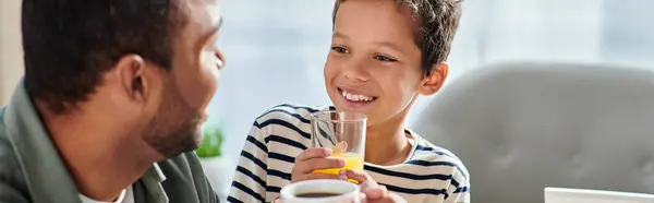 Jolly carino ragazzo africano americano con succo d'arancia sorridente a suo padre con caffè, banner — Foto stock