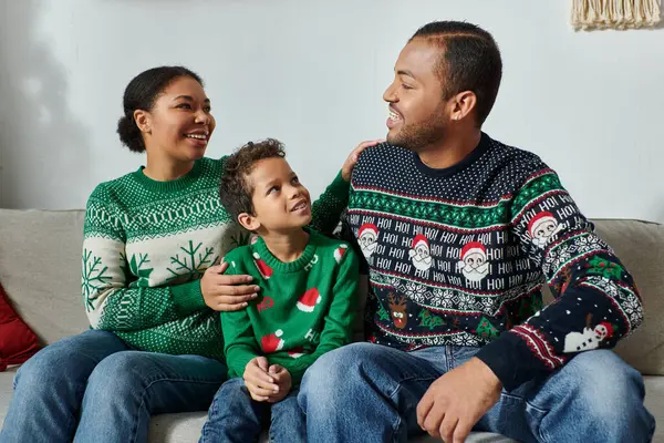 Heureuse famille afro-américaine dans des pulls confortables assis sur le canapé se souriant, Noël — Photo de stock