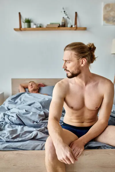 Hombre barbudo trastornado en calzoncillos sentado en la cama cerca de dormir pareja de amor, relación problemática - foto de stock