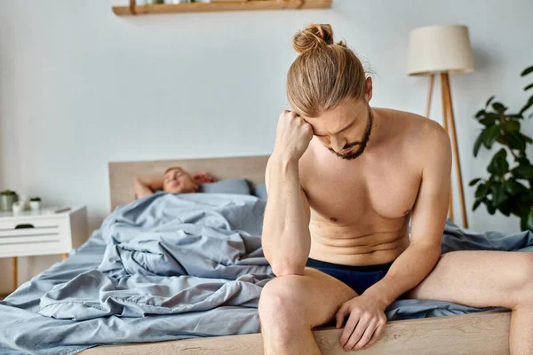 Upset bearded man in underpants sitting on bed near sleeping love partner, troubled relationship — Stock Photo
