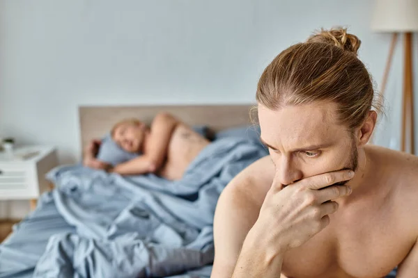 Ображений бородатий гей чоловік з рукою біля обличчя біля хлопця спить у спальні, розчарування — стокове фото