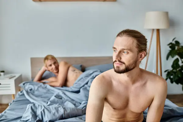 Homme barbu rêveur et positif regardant loin près partenaire gay couché sur le lit, le bonheur et la sérénité — Photo de stock