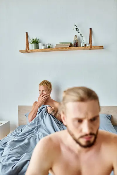 Preocupado gay hombre cubierta boca con mano cerca ofendido novio en borrosa primer plano en dormitorio - foto de stock